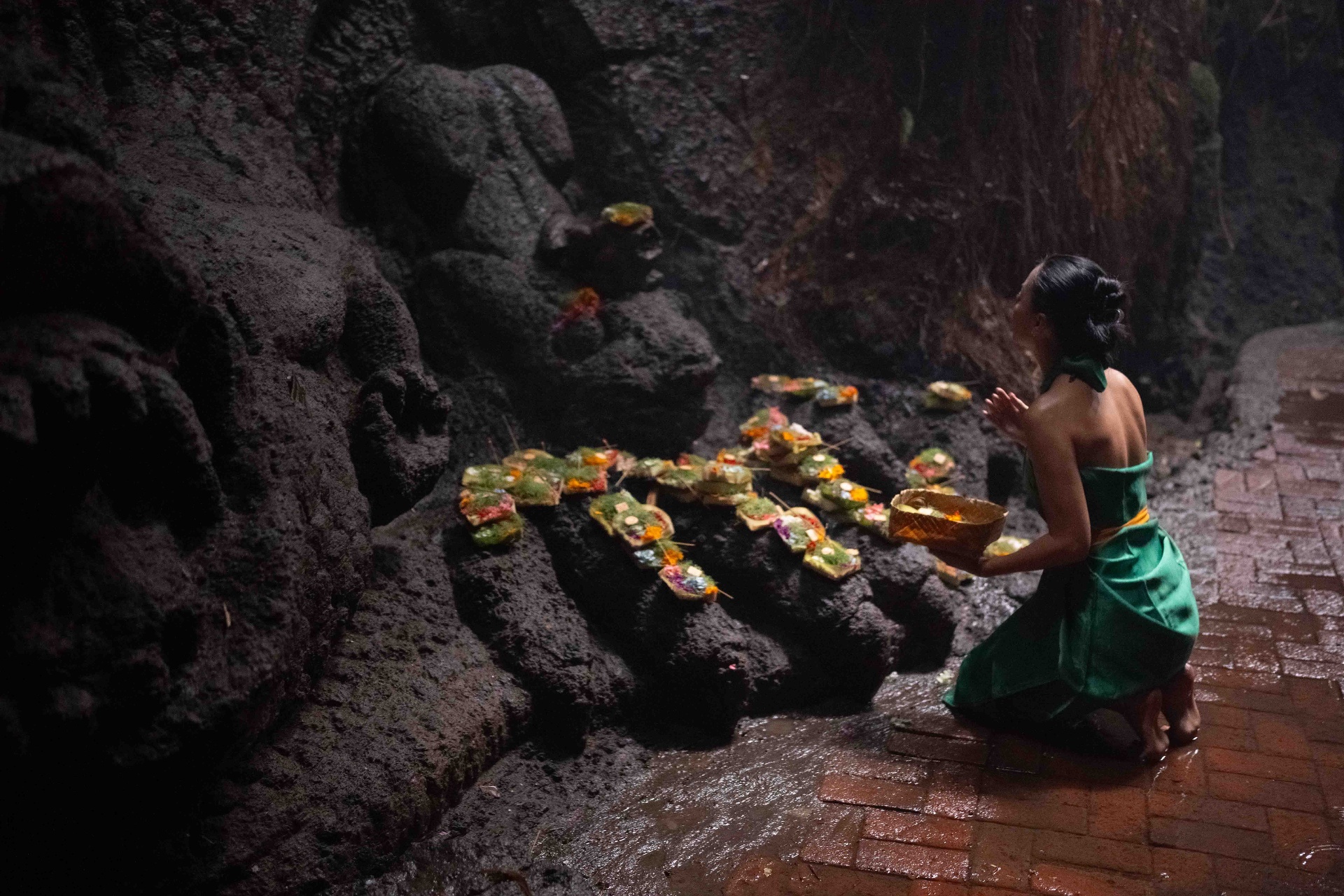 Woman kneeling in a sacred cave with floral offerings
