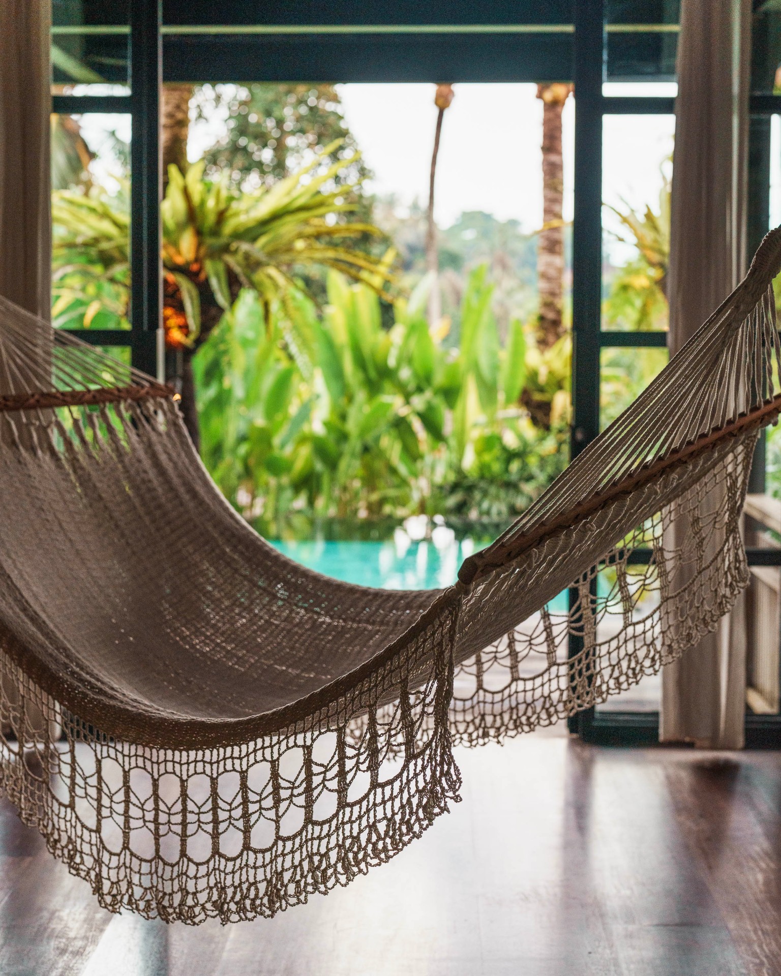 Woven hammock framing a private pool and tropical garden — arrival at the estate