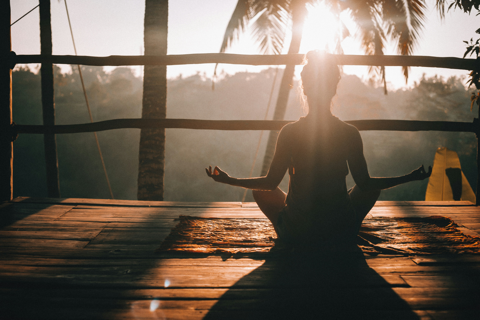 Silhouette of a woman in lotus seat at sunrise on a timber deck — guided breathwork