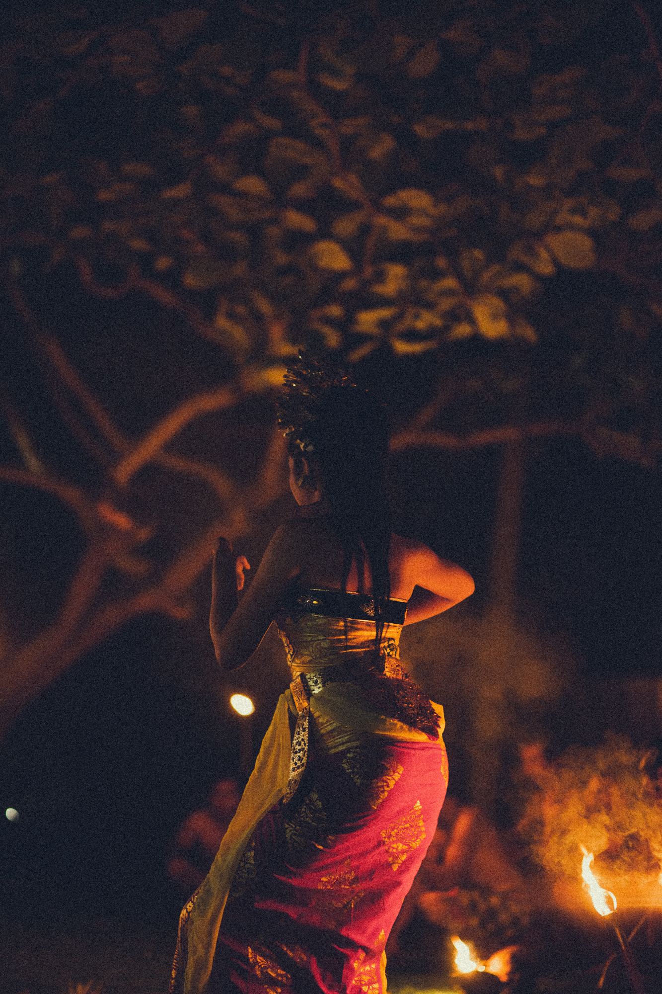 Balinese dancer in traditional dress beside firelight at night