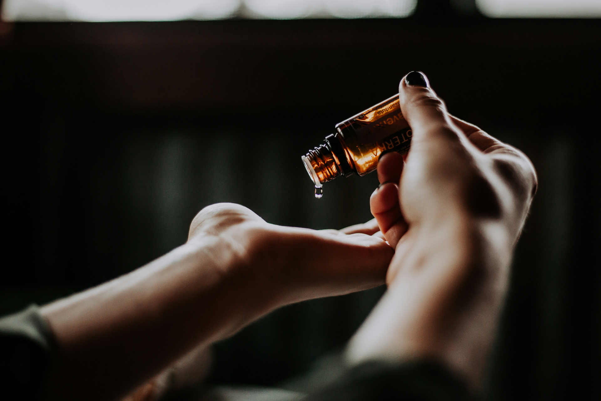 Hands dropping essential oil into an open palm in soft light